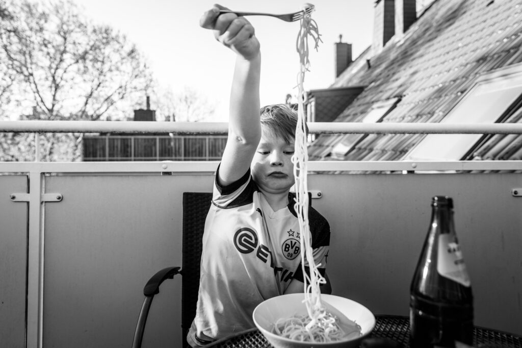 Kind versucht Spaghetti zu essen und zieht die Nudeln mit der Gabel in die Luft