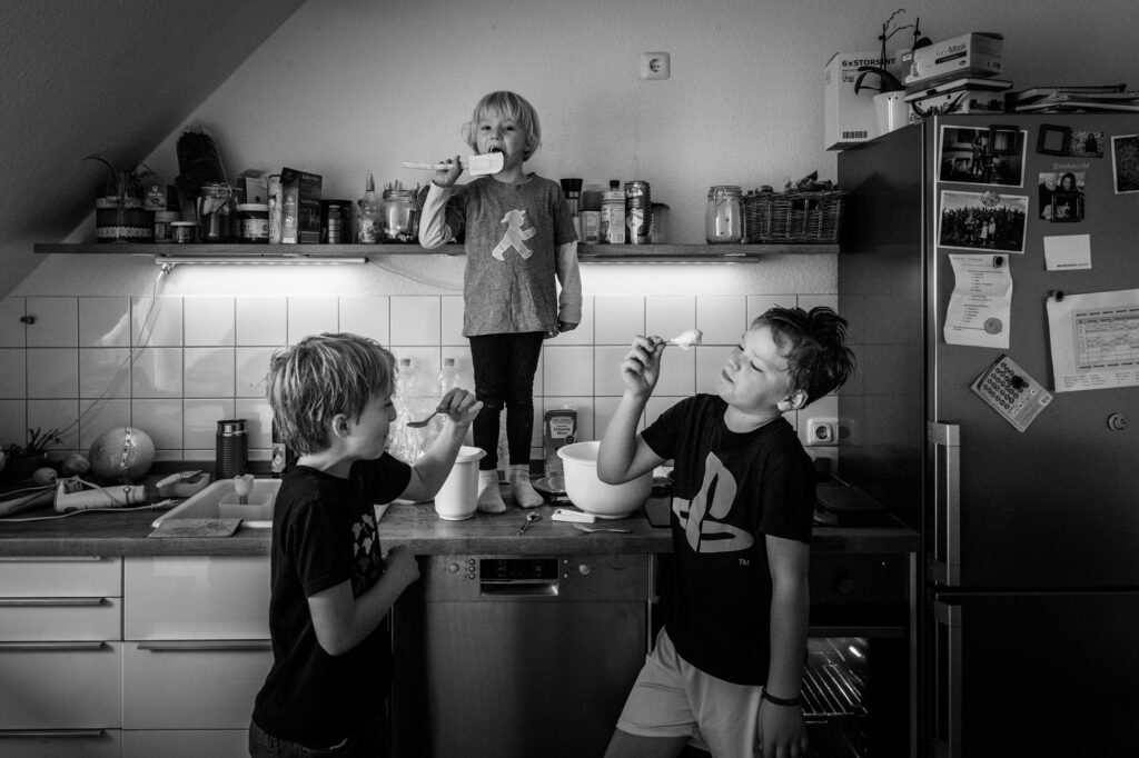 drei Kinder stehen in der Küche und naschen Kuchenteig