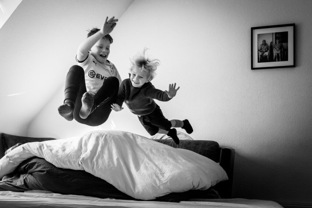 zwei Kinder hüpfen von der Couch im Wohnzimmer in eine Deckenburg