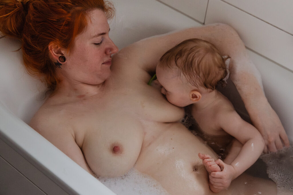 eine Mutter stillt ihr einjähriges Kind in der Badewanne