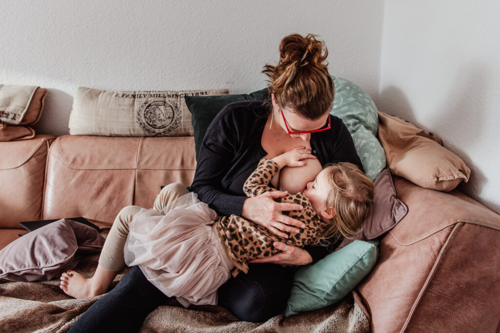 Eine Mutter sitzt auf der Couch und stillt ihr vier jährige Tochter.