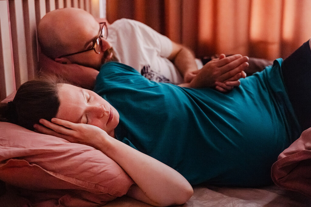 Entspannte Gebärende liegt im Bett während der Geburt im Geburtshaus Unna – Partner begleitet sie