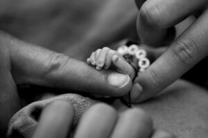 Die Hände zweier Erwachsener halten behutsam die winzige Hand eines Sternenkinds.