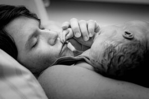 Eine Mutter küsst behutsam die Finger ihres Sternenkindes, das sie in ihren Armen hält.