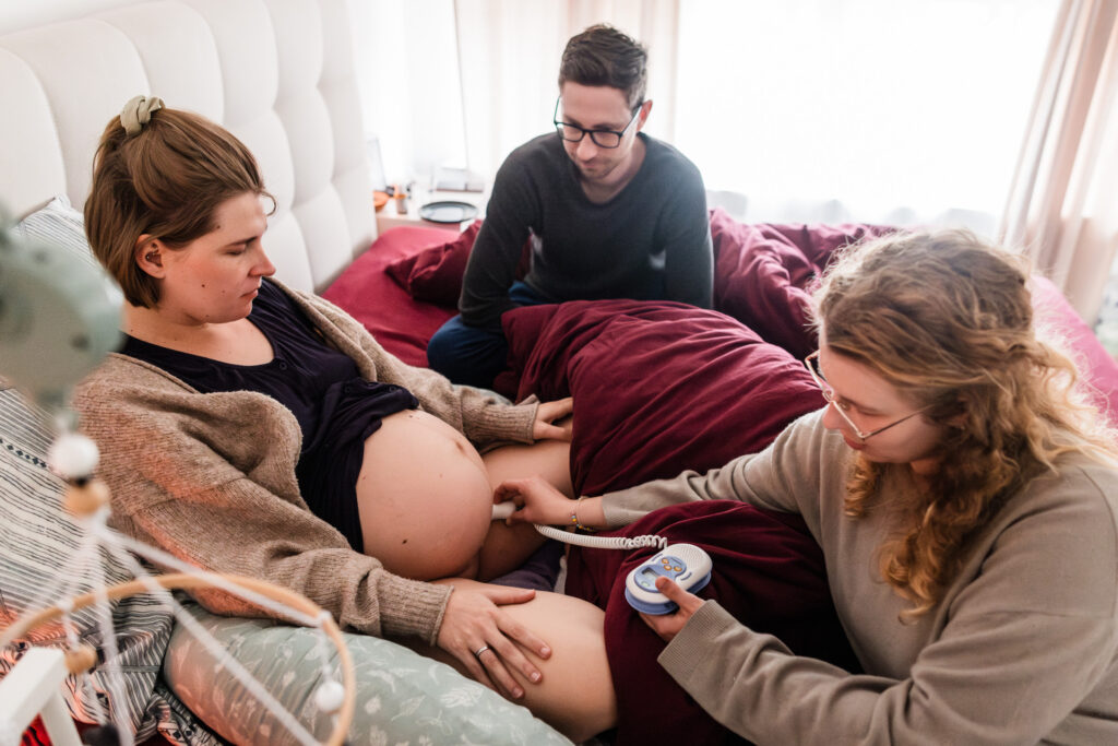 Hebamme misst die Herztöne des Babys während einer Hausgeburt in Dortmund während die Gebärende im Bett liegt